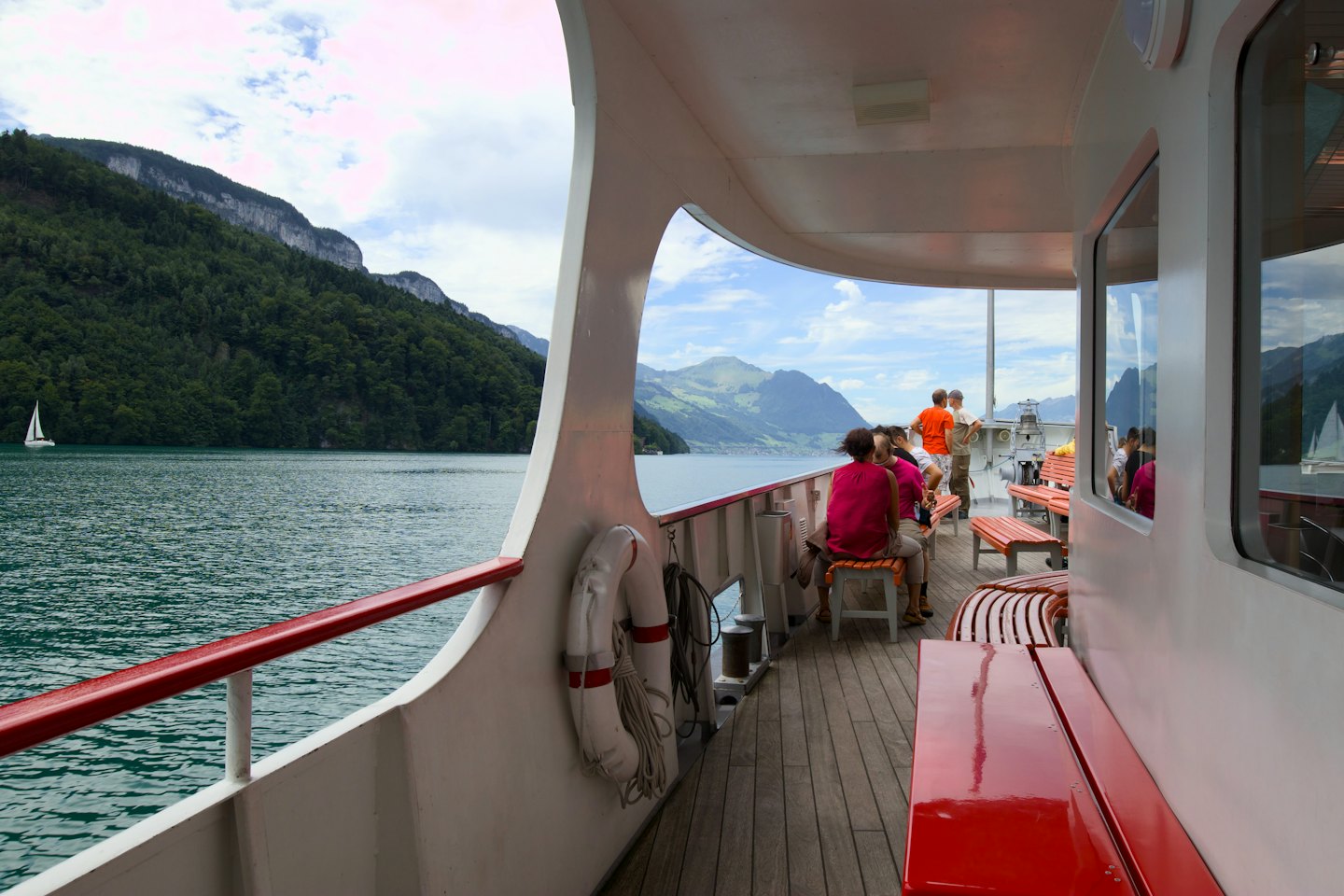 People relax on a boat deck overlooking a turquoise lake and mountains.