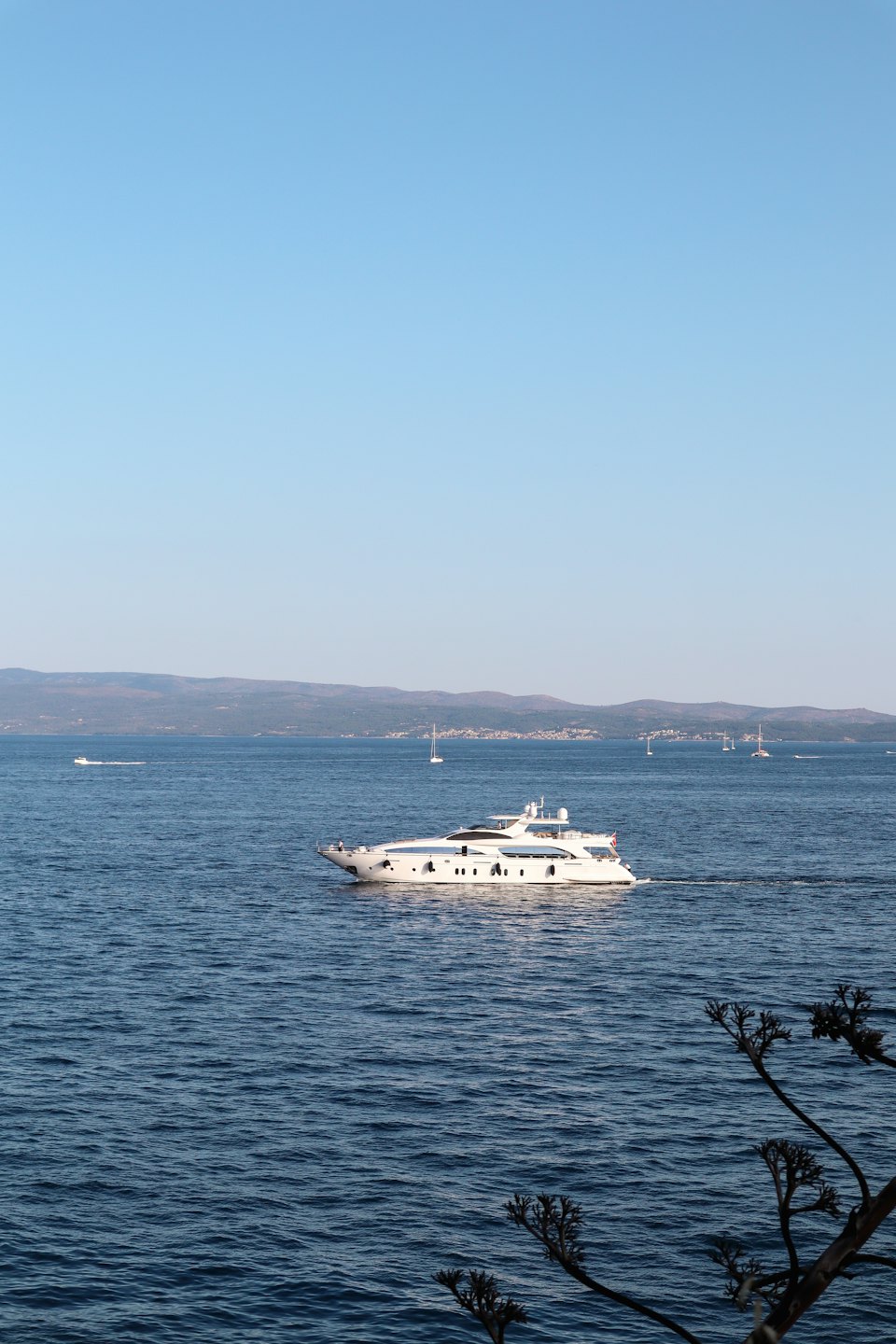 Luxury yacht sailing on calm blue water near coastline.