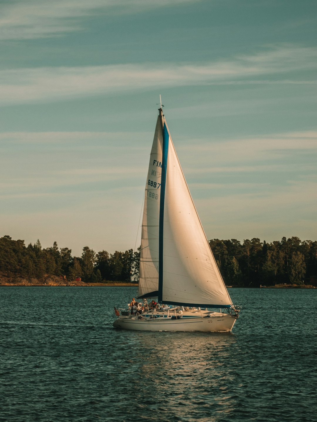 A white and blue sailboat cruises along a rocky coastline.