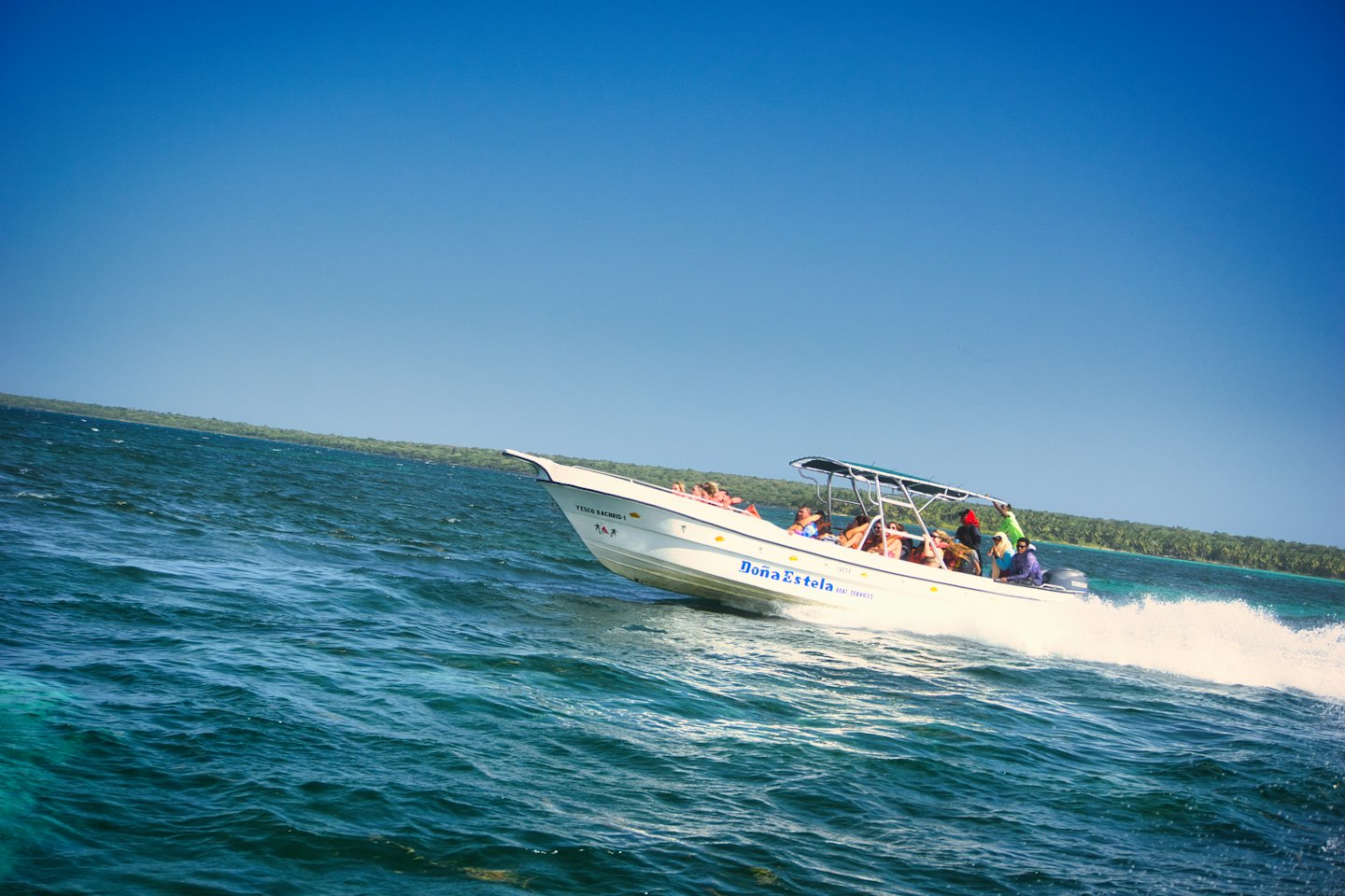 A motorboat speeds across the ocean near a tropical coastline.