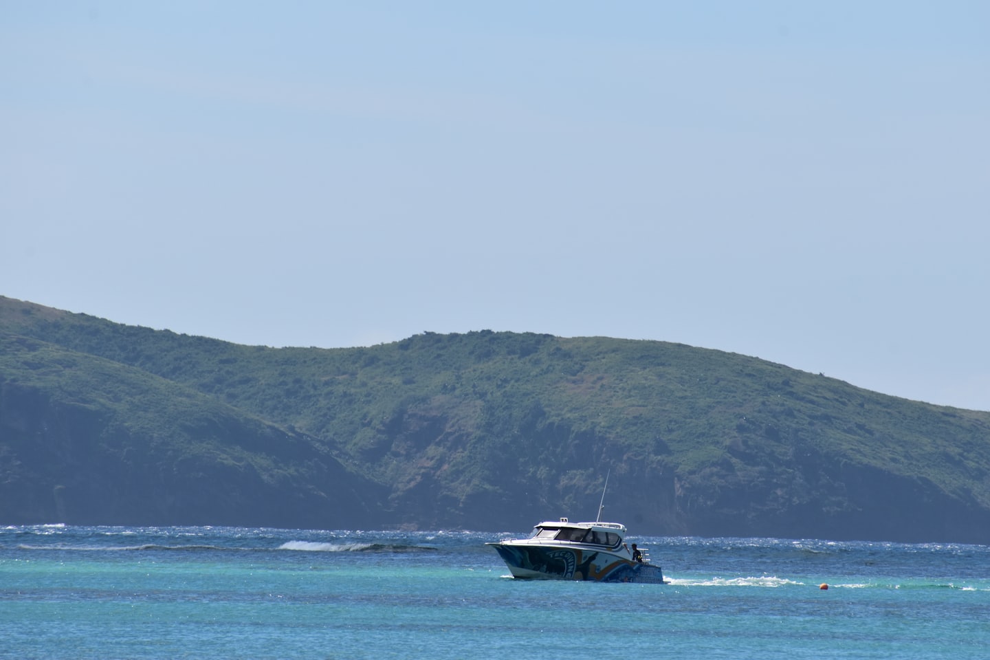 Speedboat with decorative hull on turquoise ocean near green hills.