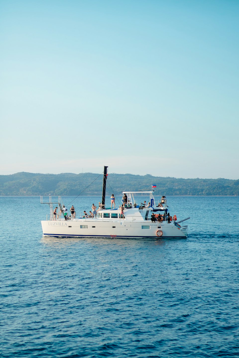 People in swimwear relax on the catamaran Luzvilla sailing across the ocean.